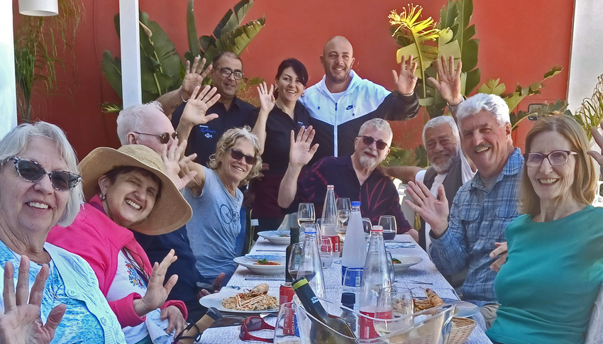 a group of people around a dining table, waving and smiling.